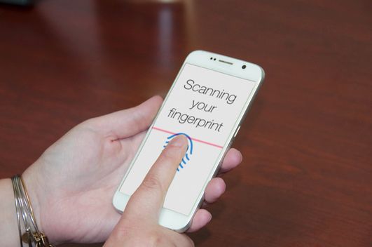 An image of someone placing their finger on a phone screen to be scanned as prompted by the device.